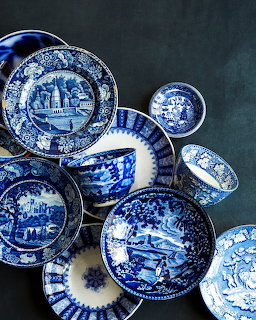 Collection of blue and white transferware plates, saucers, and cups with scenic designs on dark background