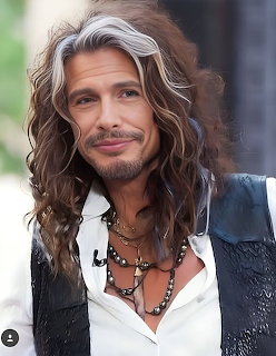 Portrait of Steven Tyler with long wavy hair, necklaces, white shirt, and black vest