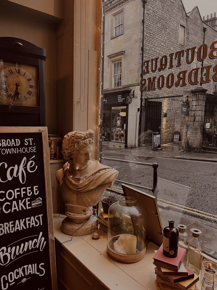Cafe window with classical bust, chalkboard menu listing coffee and brunch, overlooking a rainy street
