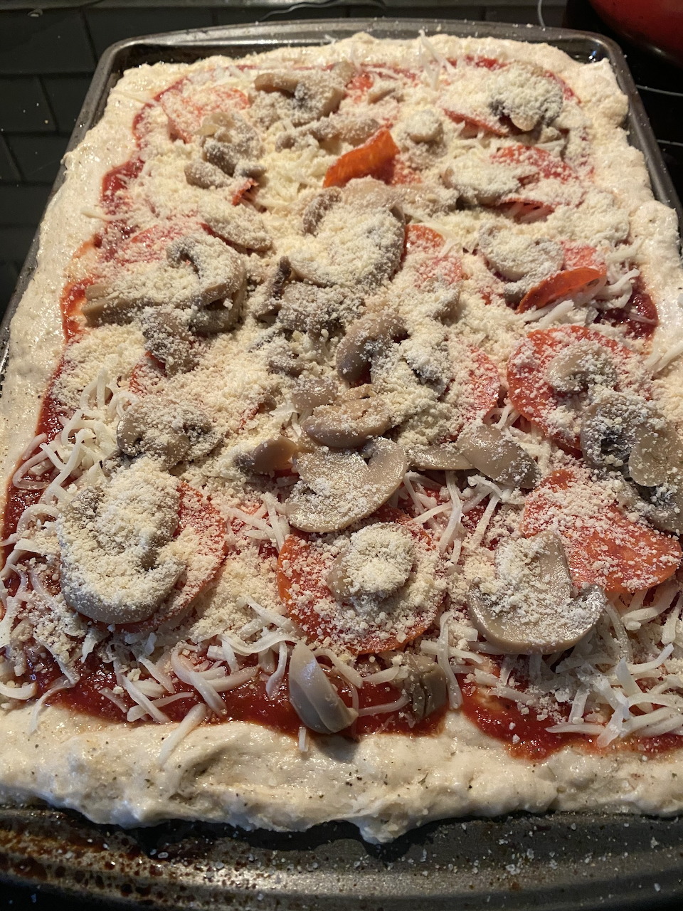 Raw homemade pizza topped with sliced mushrooms and cheese on a metal baking sheet