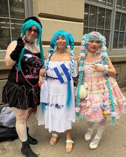 Three people in Hatsune Miku cosplay with teal twin-tail wigs posing outdoors at a convention