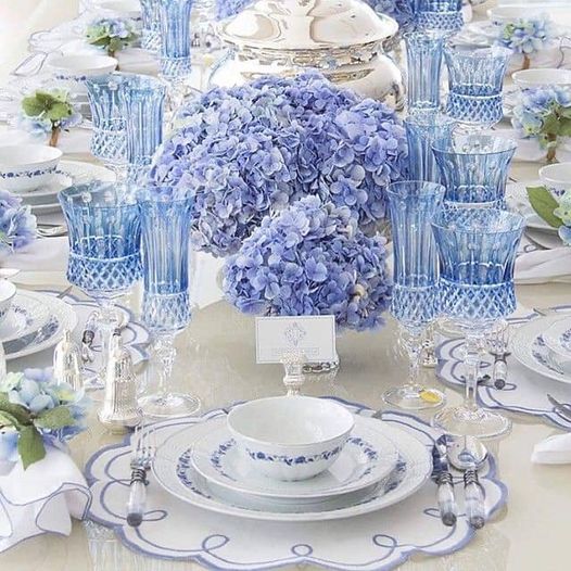 Formal tea table with blue hydrangeas, white dishes, and crystal glasses