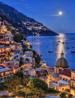 Positano Italy coastal village lit up at night with full moon over the sea
