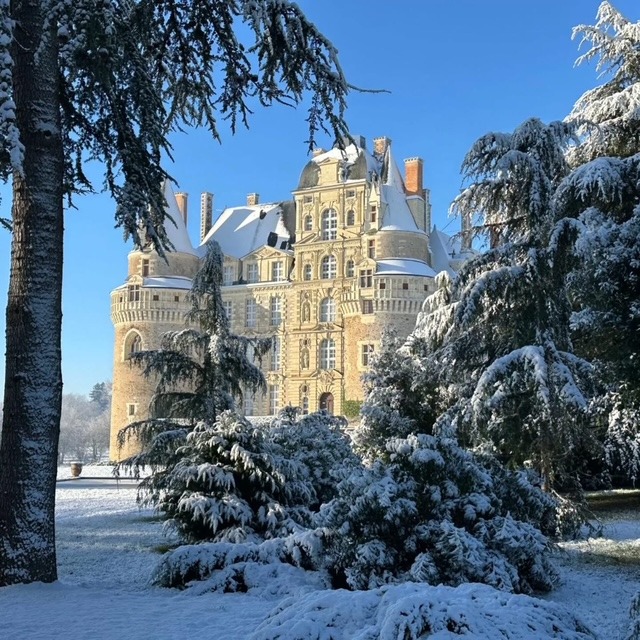 Snow-covered Chateau de Brissac behind frosted trees on a clear winter day