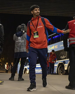 Soccer player in red tracksuit walking at nighttime stadium arrival