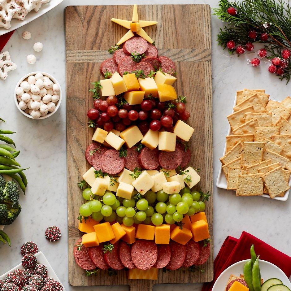 Charcuterie board shaped like a Christmas tree with meats, cheeses, and fruits on wooden board with holiday decor