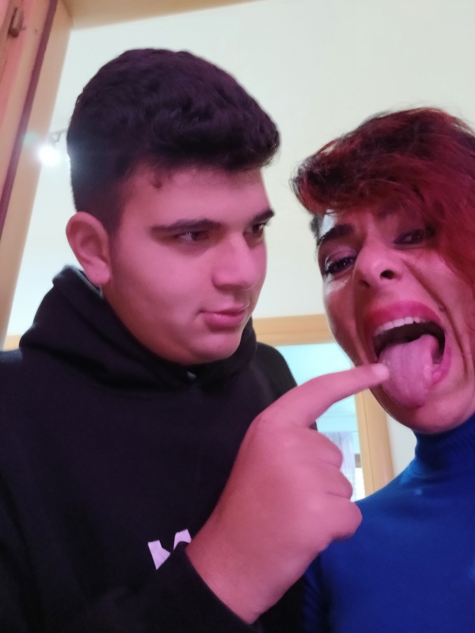 Young man pointing at a woman sticking out her tongue in a playful indoor selfie