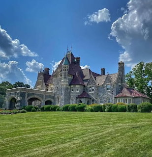 Large Gothic stone mansion with turrets and arched entrance on green lawn under blue sky
