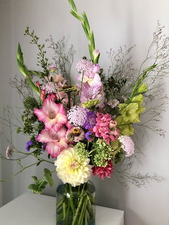 Colorful mixed flower bouquet with pink, yellow, and white blooms in glass vase on white surface
