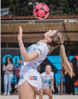 Female athlete in a white uniform balancing a pink ball during an outdoor game