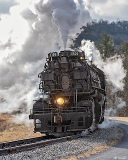 Black steam locomotive 1309 approaching on tracks with large clouds of white steam billowing above