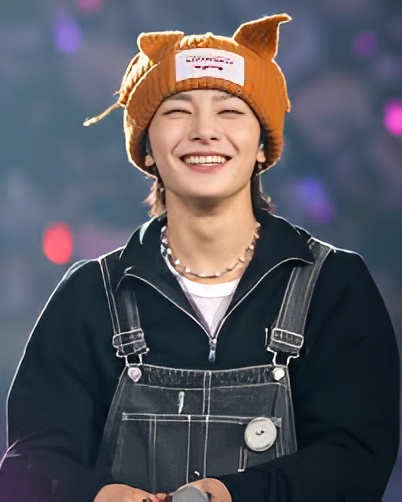 Young man smiling warmly in an orange fox-ear beanie and black denim overalls