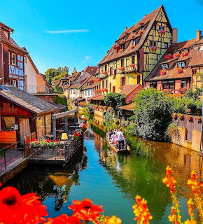 Colorful half-timbered buildings along a canal in Colmar with flowers and a boat on the water