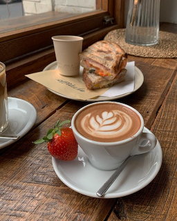 Cappuccino with latte art, sandwich, and strawberry on wooden café table