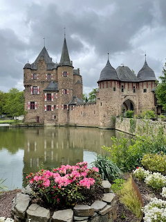 Medieval stone castle with pointed towers beside a moat with colorful flower gardens in the foreground