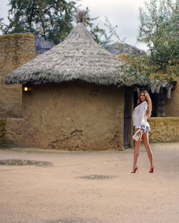Woman in white dress standing in front of a round thatched-roof mud hut