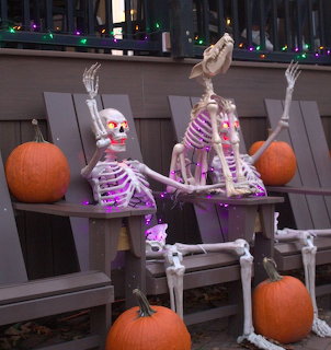 Two skeleton figures on a bench with a skeleton dog and pumpkins in a Halloween decoration display