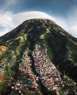 Village on the green slopes of an Indonesian volcano beneath a white cloud cap