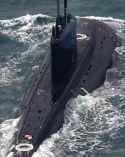 Black military submarine moving through ocean water creating white wake