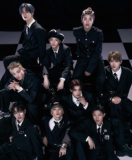 Eight xikers members in black suits posing on a checkerboard floor against a dark background.