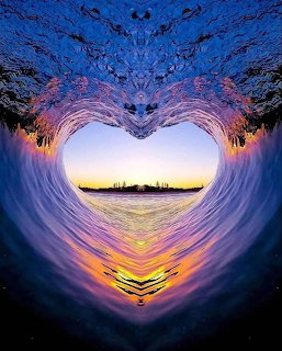 Heart-shaped tunnel formed by symmetrical ocean waves framing a sunset over water