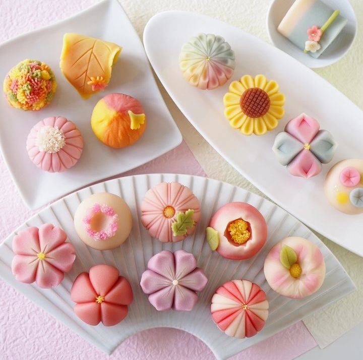 Assorted pastel-colored flower-shaped desserts and pastries arranged on white rectangular plates