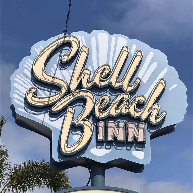 Retro Shell Beach Inn sign on a shell-shaped board against a blue sky