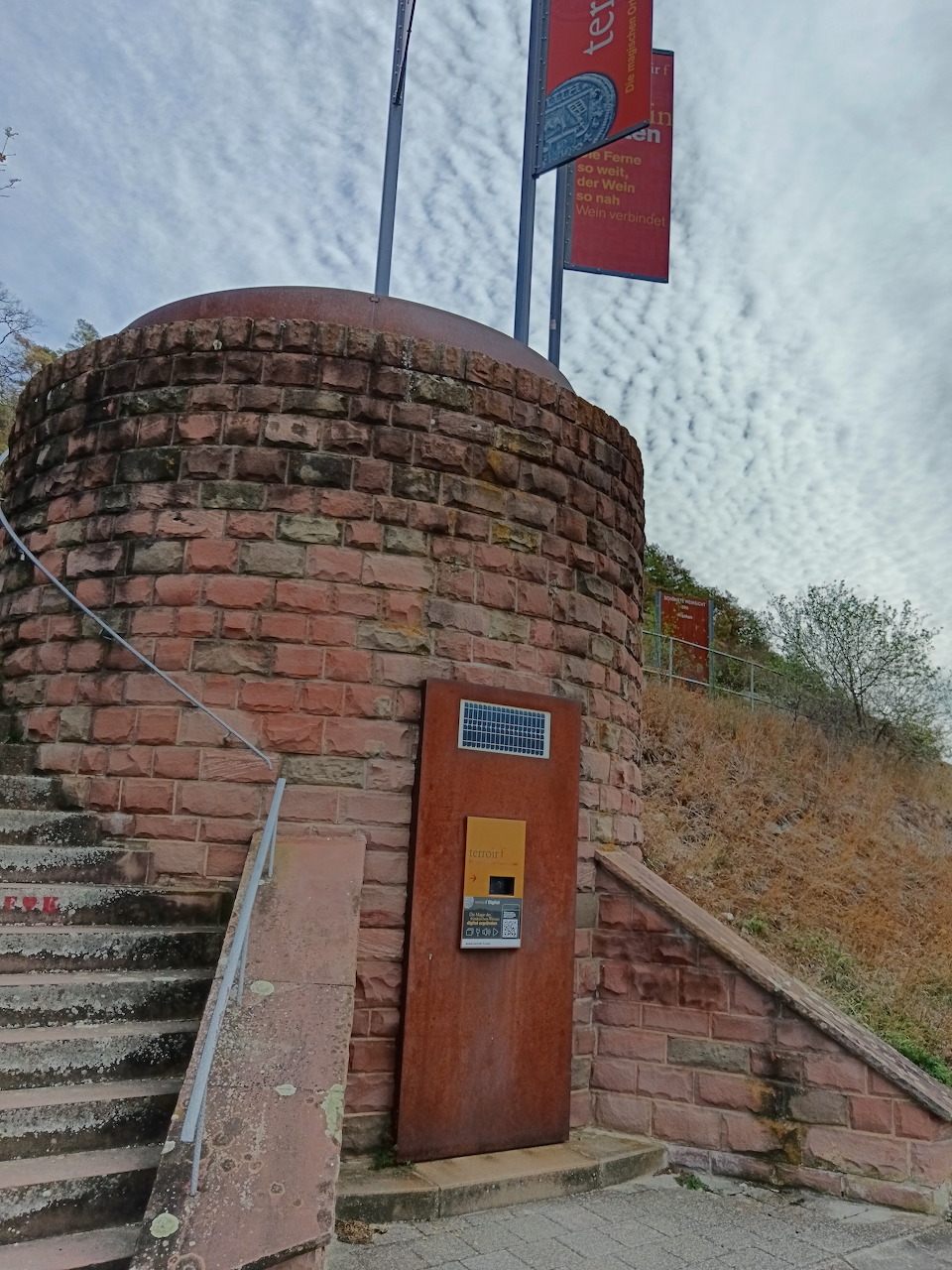 Curved red-brick structure with a wooden door and stone steps under a cloudy sky.