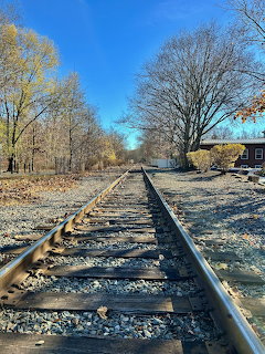 Railroad tracks vanishing into distance with bare trees and blue sky