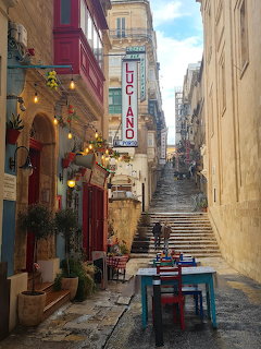 Narrow stepped street in Malta with cafe tables, hanging lights, and limestone buildings