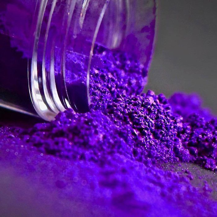 Purple glitter pouring from clear glass jar onto dark surface