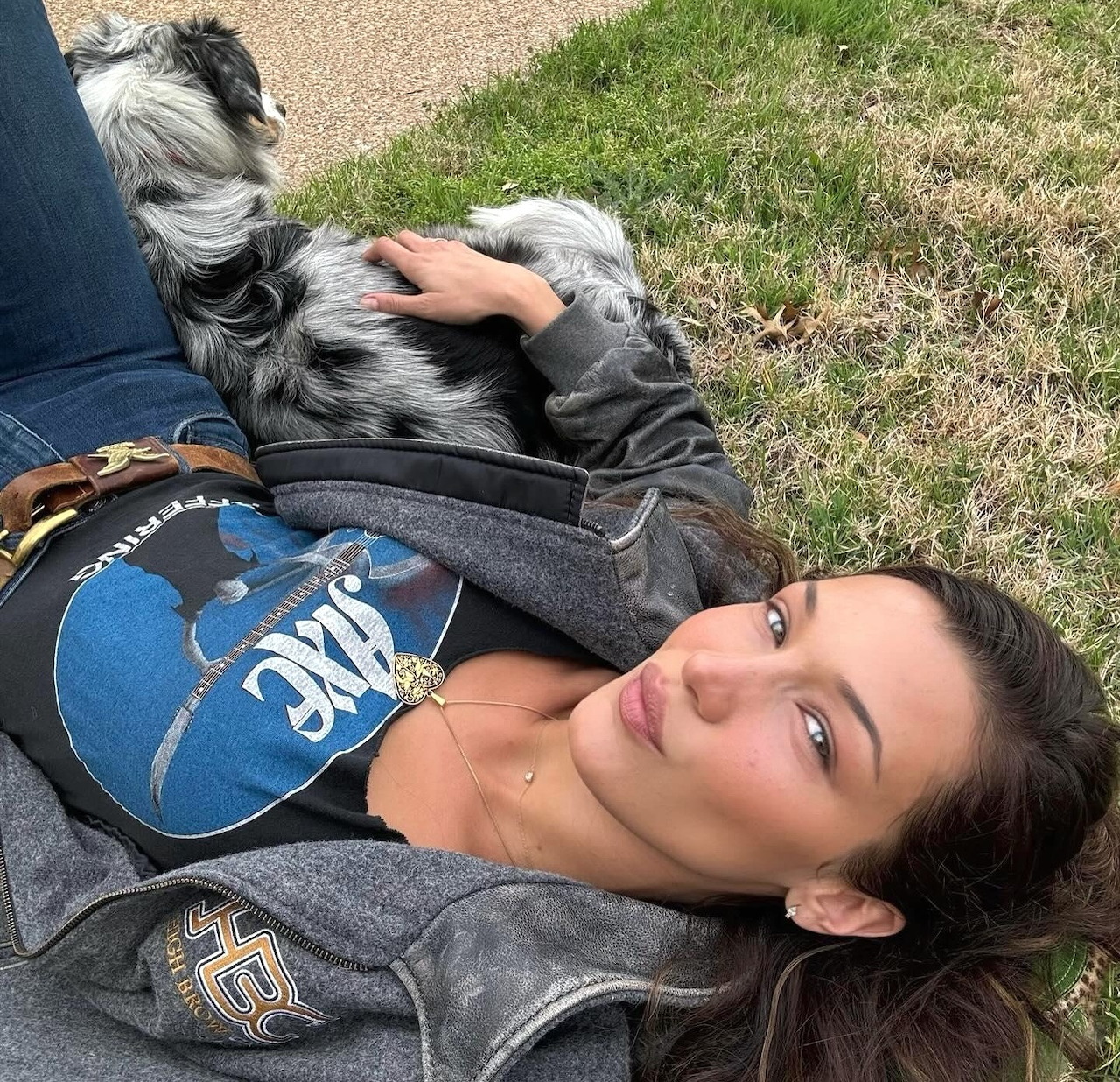 Woman lying on grass with small dog on her chest