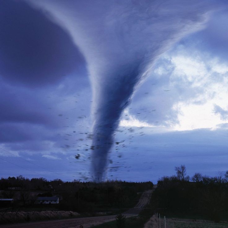 Tornado funnel cloud touching down in rural landscape under stormy sky