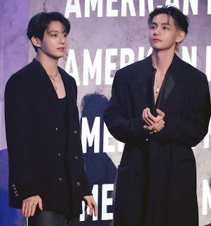 Two young Korean men in dark navy coats standing side by side at a formal event