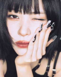 Close-up of a winking woman with black bob hair and decorated nails resting her face on her hand.
