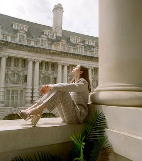 Woman in beige sweater sitting beside white column with classical architecture behind