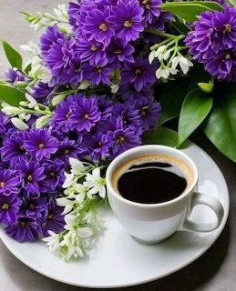 Purple and white flowers next to a cup of coffee on a white saucer