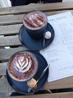 Two cups of latte on a wooden cafe table with a printed menu and spoons