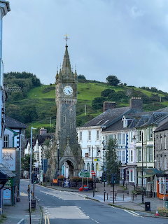 Stone clock tower in the center of Machynlleth town street with buildings and green hill behind