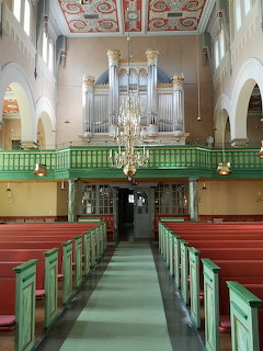Interior of Nora church showing green balcony with pipe organ, chandelier, and red wooden pews