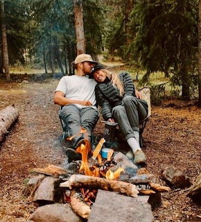 Couple sitting on a log by a campfire in a pine forest