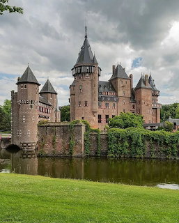 De Haar Castle in the Netherlands with towers, moat, and green lawn under cloudy sky
