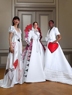 Three women in white haute couture gowns with red heart details and ruffled embellishments in elegant room