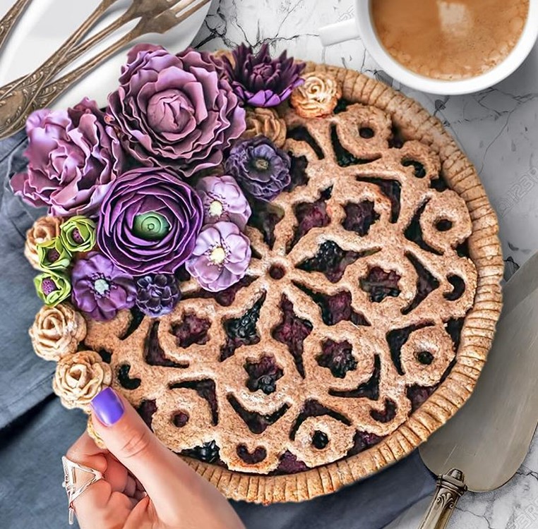 Berry pie with ornate lattice top and purple flower decoration beside coffee cup