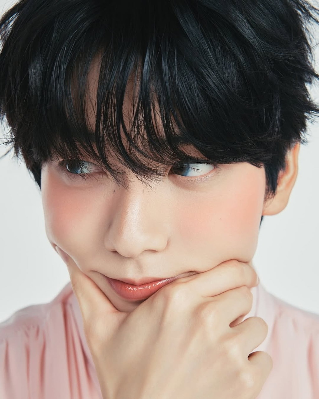Young person with short black hair and rosy cheeks resting chin on hand, looking sideways