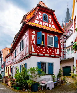 Red half-timbered house with white walls in historic German town, church spire in background