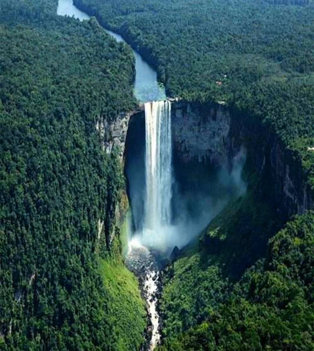 Aerial view of a massive waterfall dropping into a rainforest gorge surrounded by dense jungle