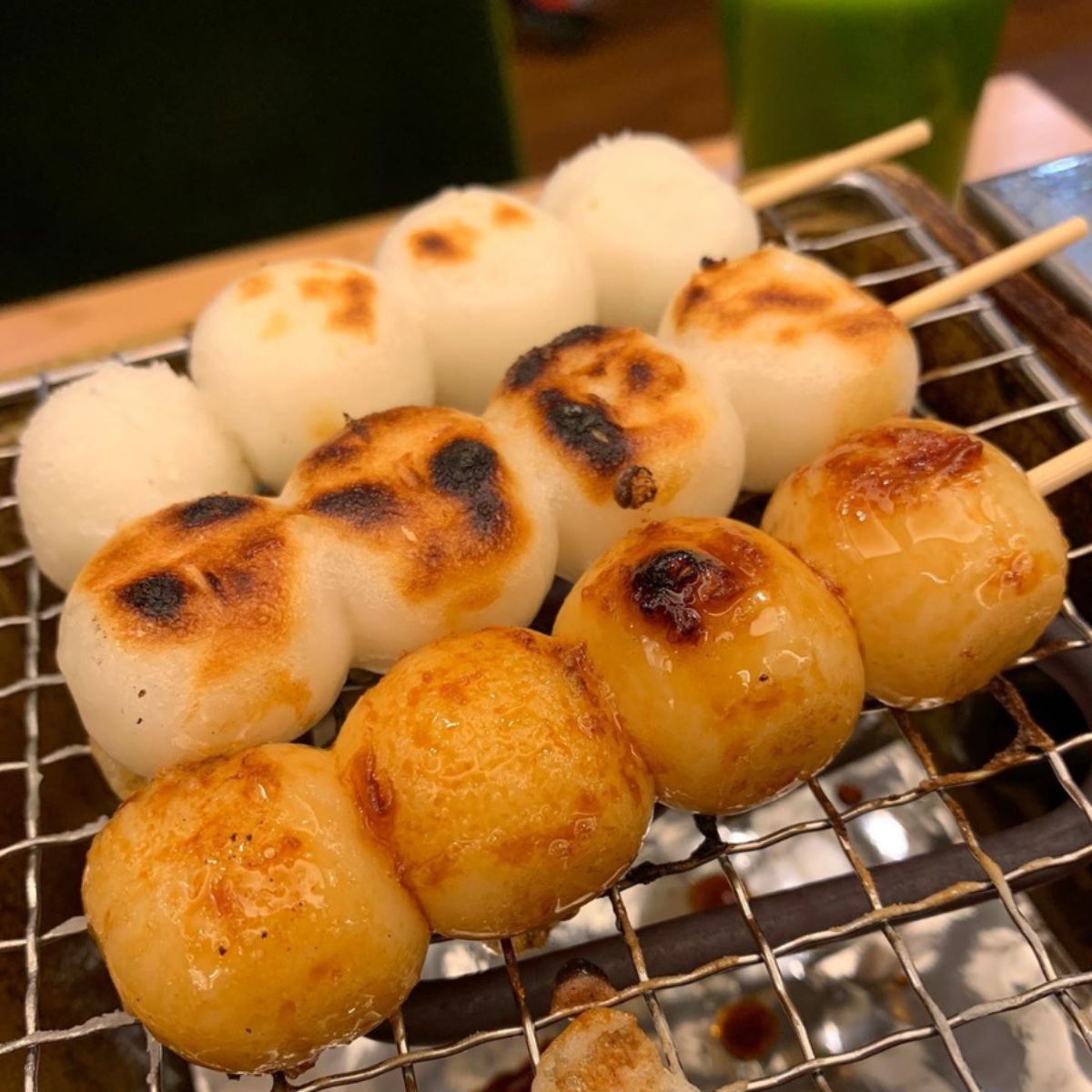Skewered dango rice balls grilling on a wire rack with charred golden surfaces