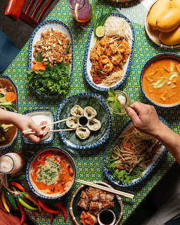 Overhead flatlay of Middle Eastern food spread with colorful dishes, grilled meats, fresh herbs and hands reaching for food