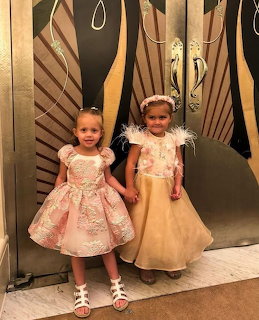 Two young girls in fancy pink dresses holding hands indoors